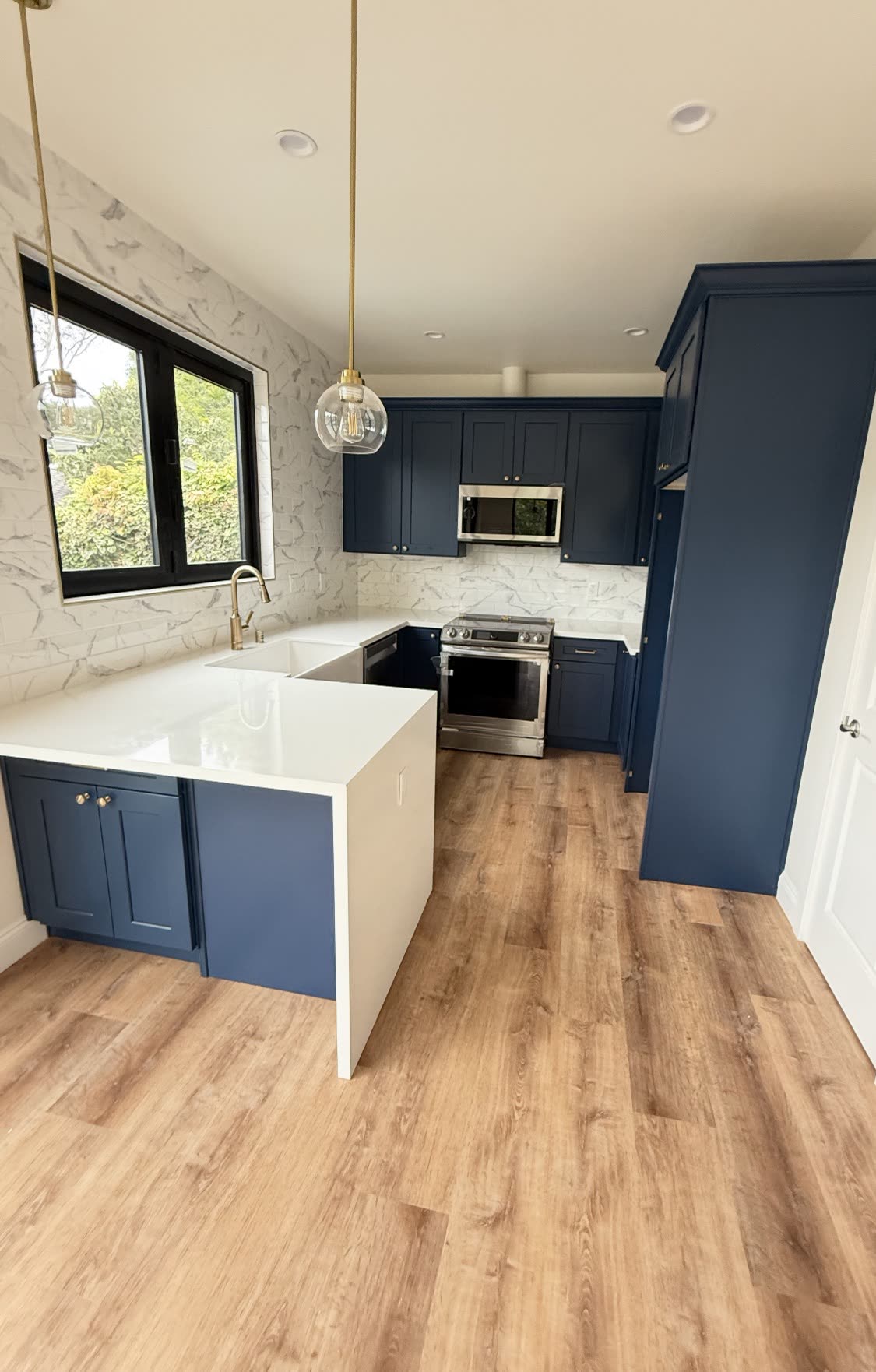 Remodeled kitchen with navy shaker cabinets, white quartz counters and brass fixtures