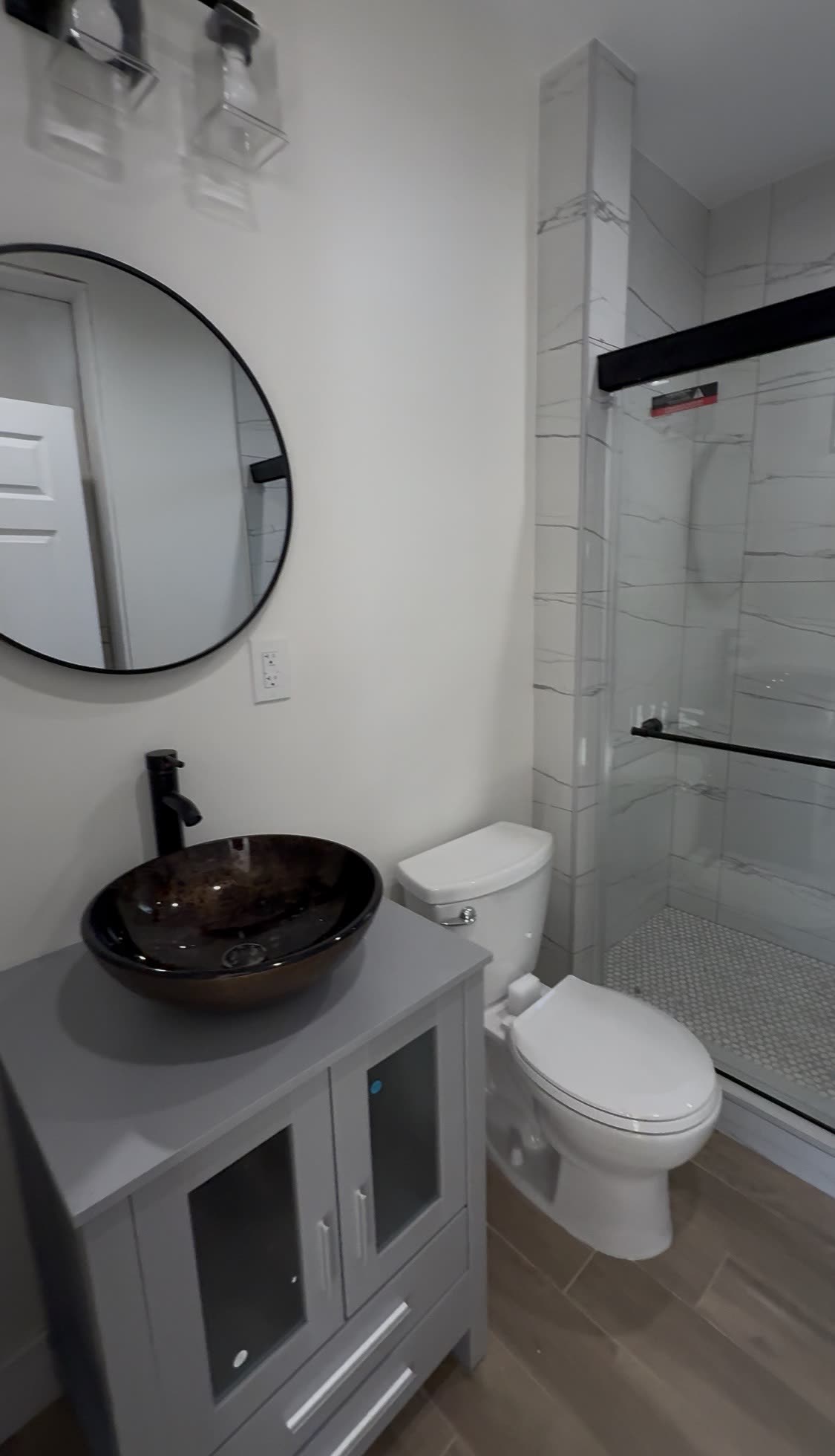 Bathroom with gray vanity, black vessel sink and marble walk-in shower